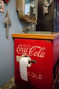 an old coca - cola machine is painted red and has a roll of toilet paper on it