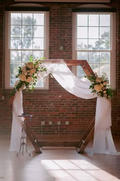 an arch decorated with flowers and greenery stands in front of two windows at the end of a wedding ceremony