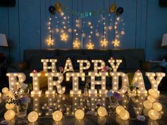 a happy birthday sign made out of lighted letters on a wooden table with flowers and candles