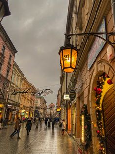 people walking down the street in an old european town at christmas time with lights and decorations