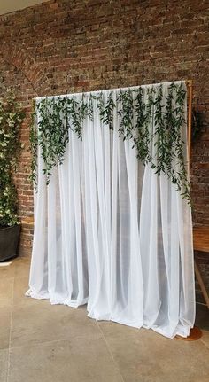 a brick wall with white sheer curtains and greenery on it