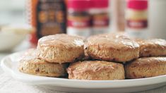 a white plate topped with biscuits covered in glaze next to bottles of peanut butter