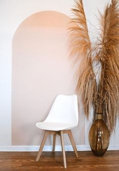 a white chair sitting next to a vase with dry grass in it on a hard wood floor