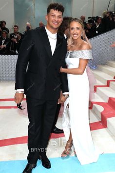 a man and woman standing next to each other on a blue carpet with people in the background