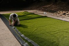 a man kneeling down on top of a lush green field next to a wooden fence