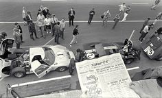 a group of people standing around cars in a parking lot next to a man holding up a paper