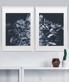 two black and white pictures hanging on the wall next to a vase with a cactus in it