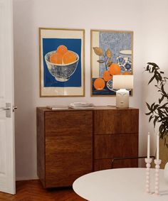 two framed oranges are on the wall above a wooden cabinet in this living room