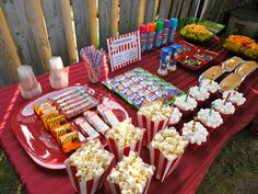 a red table topped with lots of popcorn and candy bar items on top of it