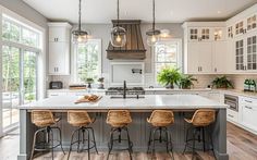 a large kitchen with white cabinets and wooden flooring is pictured in this image, there are four stools at the center of the island