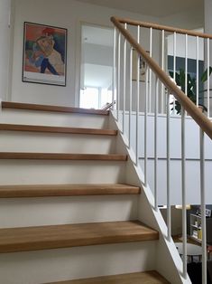 there is a painting on the wall next to the stairs in this room with wood floors and white railings