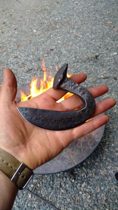 a hand holding an iron hook over a fire pit with it's flame coming out