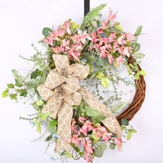 a wreath with pink flowers and greenery hanging on a door hanger in front of a white wall