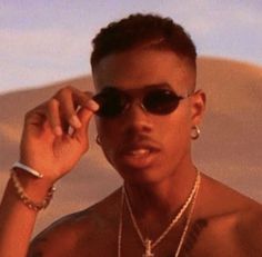 a man wearing sunglasses and holding his hand up to his face while standing in the desert