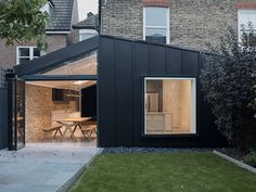 a black house with an open patio and dining table in the back yard, next to a brick building