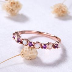 a pink gold ring with white and purple stones on the side, surrounded by dried flowers