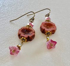 "Lovely little pink dangles featuring 15 mm pink Czech glass Hawaiian flowers with rustic Picasso glaze, 6 x9 mm fuchsia pink Czech bellflowers with copper, and 6 mm pink/gold fire polished crystal rondelles. Czech beads are accented with antique gold beaded spacers and daisies. Vintage bronze French ear hooks. Total drop 2\"." Pink Round Earrings With Flower Charm, Vintage Pink Nickel-free Flower Earrings, Pink Dangle Earrings With Pressed Flowers, Nickel-free Round Pink Flower Earrings, Adjustable Pink Jewelry With Pressed Flowers, Pink Flower Earrings With Adjustable Ear Wire, Round Pink Nickel-free Flower Earrings, Adjustable Nickel-free Pink Flower Earrings, Pink Adjustable Flower Earrings With Ear Wire