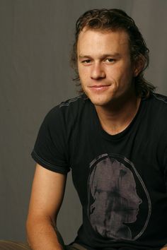 a man sitting down with his hands on his knees and looking at the camera while wearing a black t - shirt