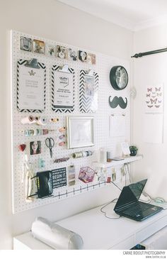 a white desk topped with a laptop computer next to a wall covered in pictures and magnets