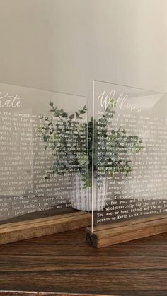 two clear acrylic vases with plants in them sitting on a wooden table