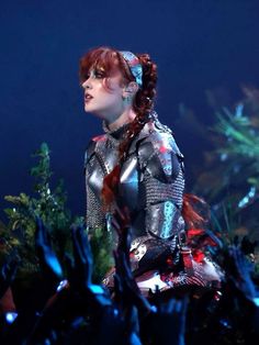 a woman with red hair and metal armor on her body in front of an audience