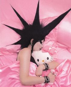 a woman laying on top of a pink bed holding a hello kitty stuffed animal in her lap