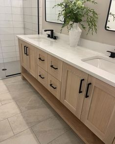 a bathroom with two sinks, mirrors and a plant in a vase on the counter