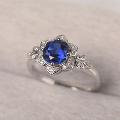 a ring with a blue stone surrounded by white diamonds on a gray surface, in the middle