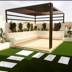 an outdoor living area with grass and white stepping stones on the ground, covered by a pergolated roof