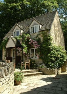 a stone house with flowers growing on it's roof and windows in the front