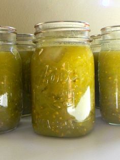 four jars filled with pickles sitting on top of a white counter next to each other