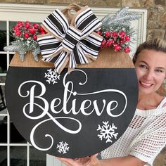 a woman holding up a black and white sign that says believe with snowflakes on it