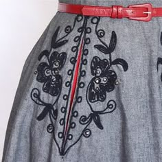 a woman's gray dress with black flowers and red trimmings on the waist