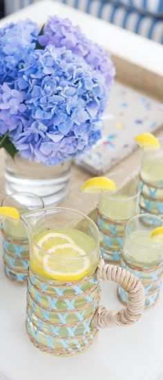 blue hydrangeas and lemons sit on a tray next to glasses with water in them