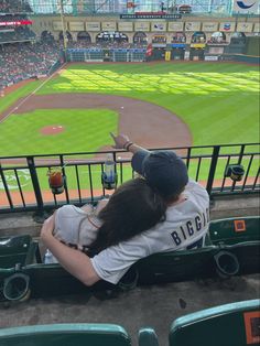 a woman sitting in the bleachers at a baseball game with her back to the camera