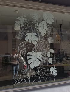 a woman is standing in front of a window with plants drawn on the glass behind her