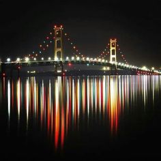 the bay bridge is lit up at night with lights reflecting in the water below it