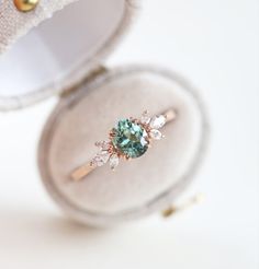 an engagement ring with a green stone and three diamonds in it sitting on a white surface