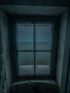 a window in an old building looking out to the ocean at night with light coming through