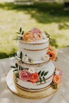 a three tiered wedding cake with flowers on the side and gold trimmings