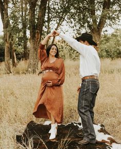 a man and woman standing on top of a log in a field next to trees