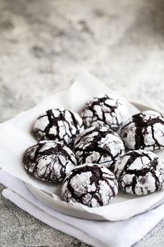 chocolate crinkle cookies sitting on top of a white plate covered in powdered sugar