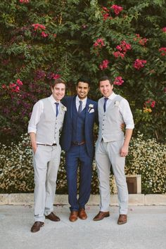 three men standing next to each other in front of flowers