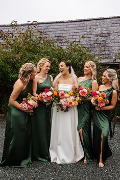 a group of women standing next to each other in front of a house holding bouquets