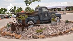 an old pick up truck is sitting in the middle of a gravel bed with plants growing out of it