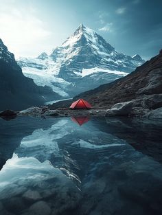 a red tent sitting on top of a mountain next to a body of water with snow covered mountains in the background