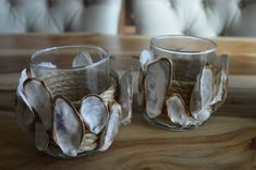 two glass cups sitting on top of a wooden table next to each other with seashells in them