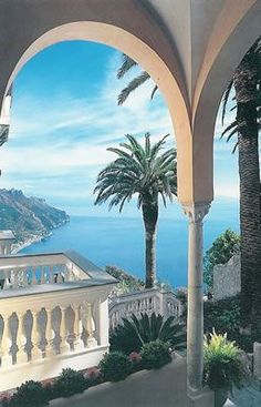 an outdoor area with palm trees and water in the background, surrounded by stone arches