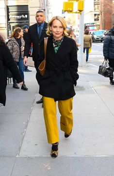 a woman is walking down the street wearing yellow pants and black coat with her hands in her pockets