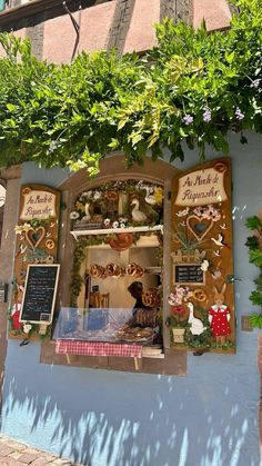 a store front with an assortment of items on display in the window and below it is a tree